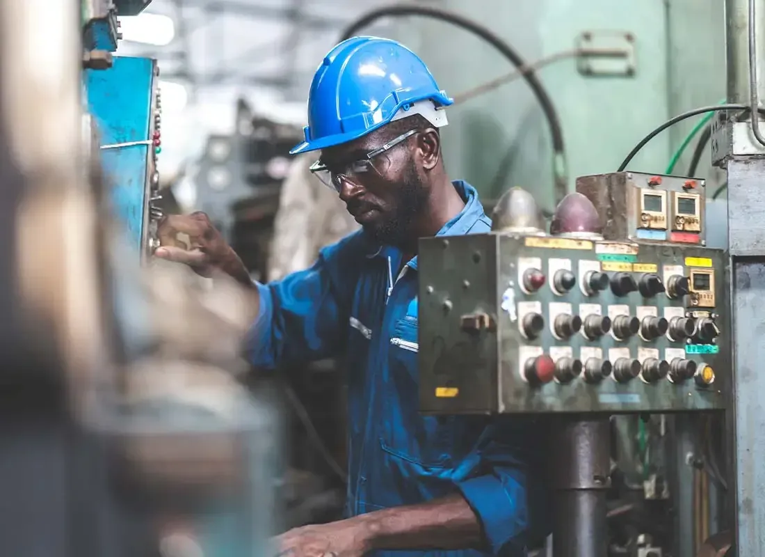 A machine operator in a hard hat and safety glasses adjusting the controls on a shop machine — machine shop and manufacturing insurance in Nebraska