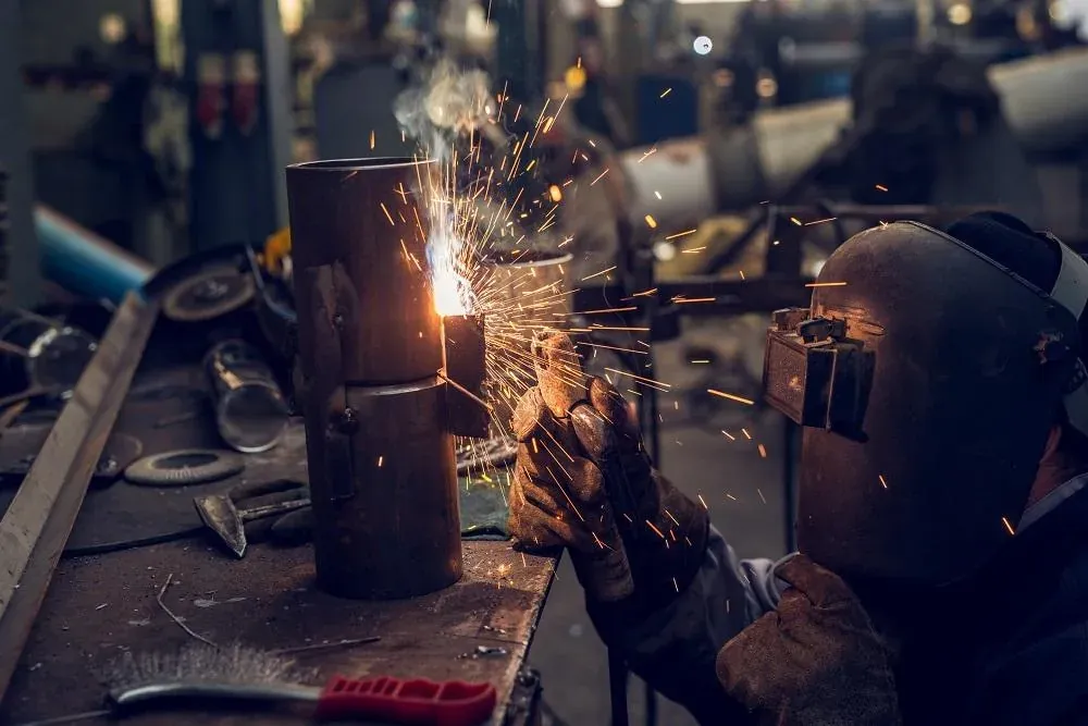 A fabricator in a welding mask joining a steel pipe as sparks fly at a workbench — machine shop and manufacturing insurance in Nevada