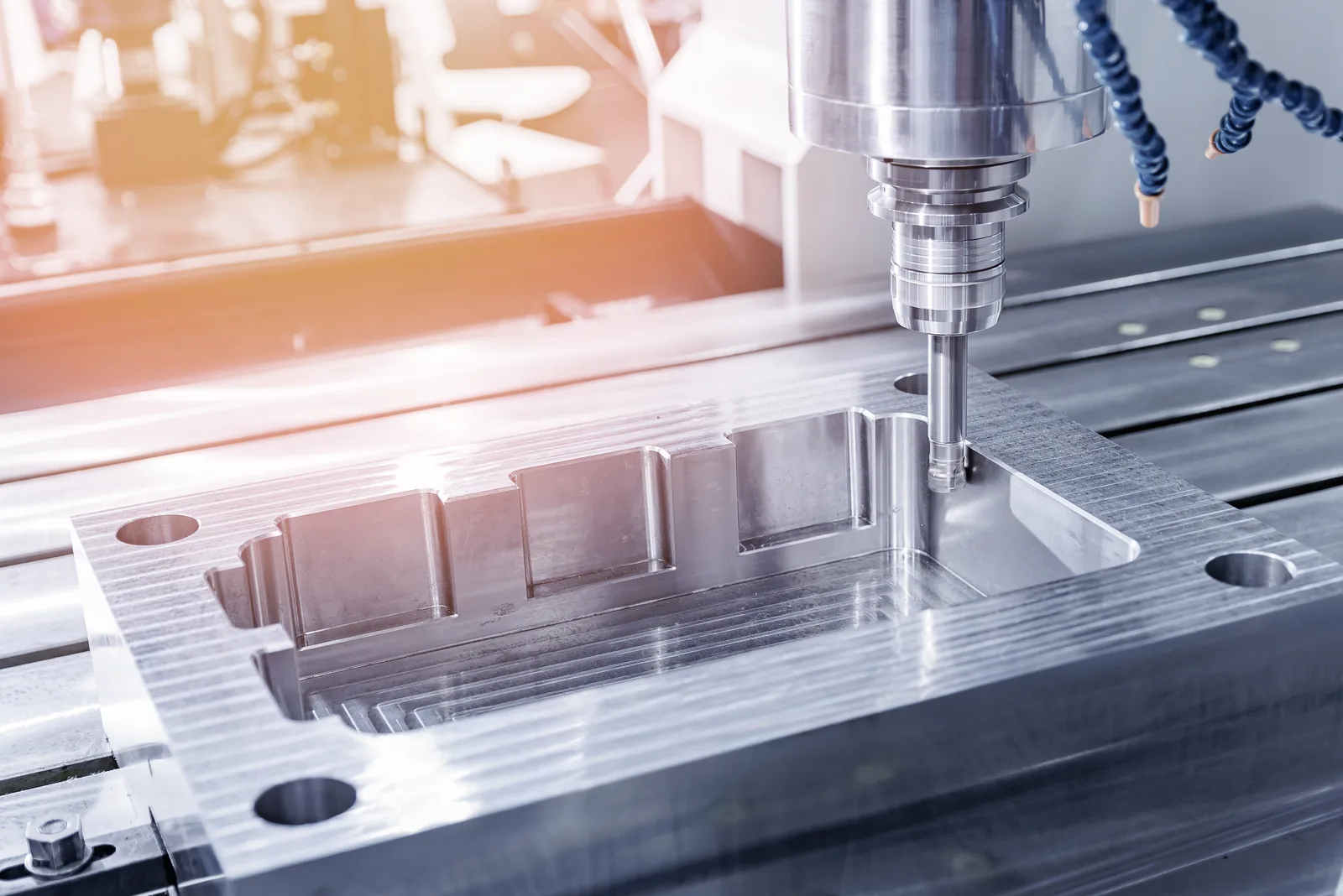 A milling machine cutting a stepped pocket into a clamped steel plate, with the shop floor lit behind it