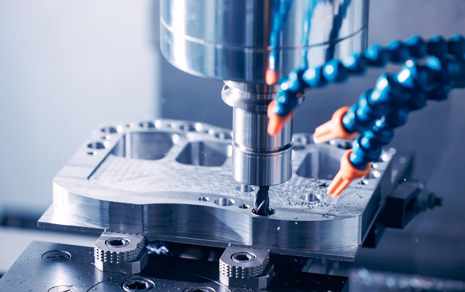 A close view of a cutting tool entering a clamped metal plate on a machine table, with chips scattered around the cut