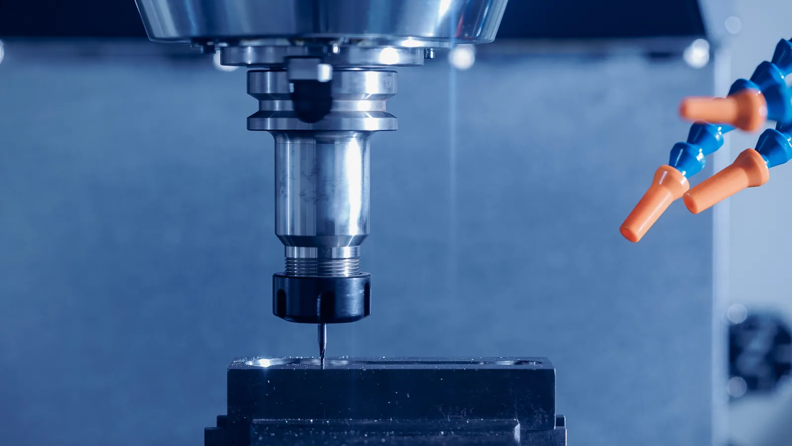 A machine spindle and collet chuck lowered toward a clamped workpiece, with coolant nozzles aimed at the tool — machine shop and manufacturing insurance in Delaware