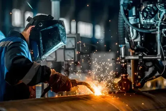 A welder in a protective helmet joining metal as sparks scatter across a fabrication shop